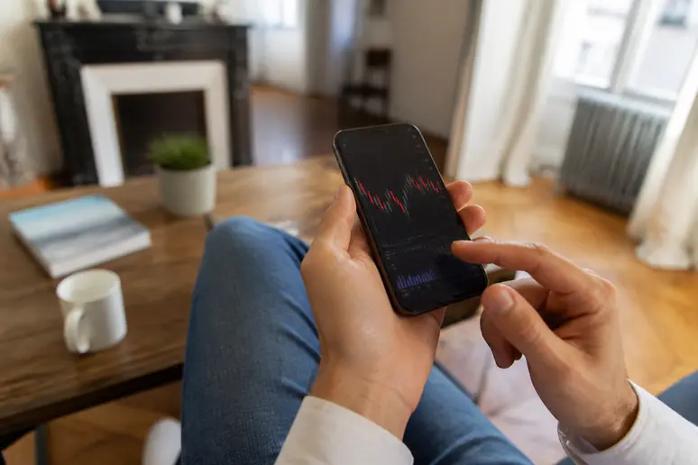 Mains d'une personne utilisant une application de finance décentralisée sur un smartphone dans un salon lumineux.