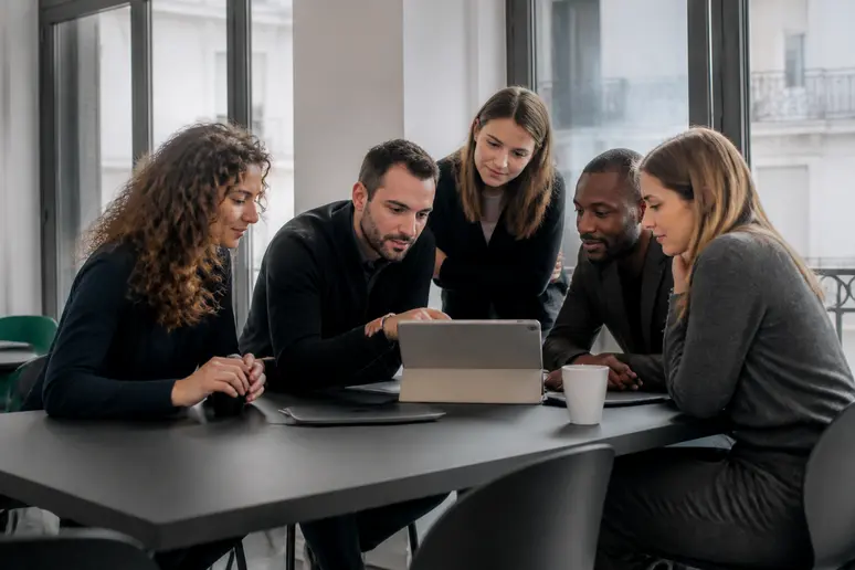 Des professionnels parisiens échangent autour d'une table, analysant des graphiques financiers sur une tablette dans un espace de coworking lumineux.
