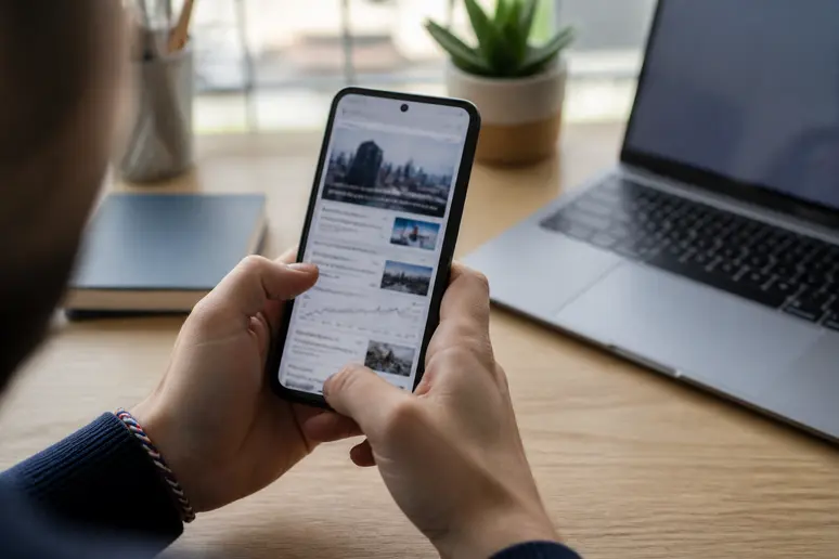 Mains tenant un smartphone affichant des informations financières, dans un contexte domestique, illustrant la réflexion sur la fiscalité des investissements.