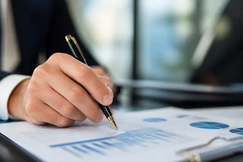 Une main tenant un stylo au-dessus d'un document financier, symbolisant la prise de décision et les implications fiscales lors de la gestion d'un Plan d'Épargne en Actions.
