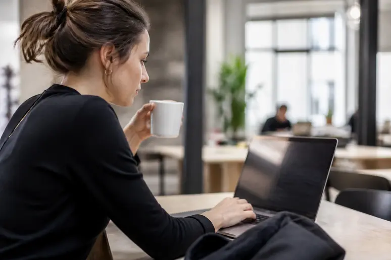 Une jeune femme française dans un espace de coworking moderne, concentrée sur son ordinateur portable affichant des données financières.
