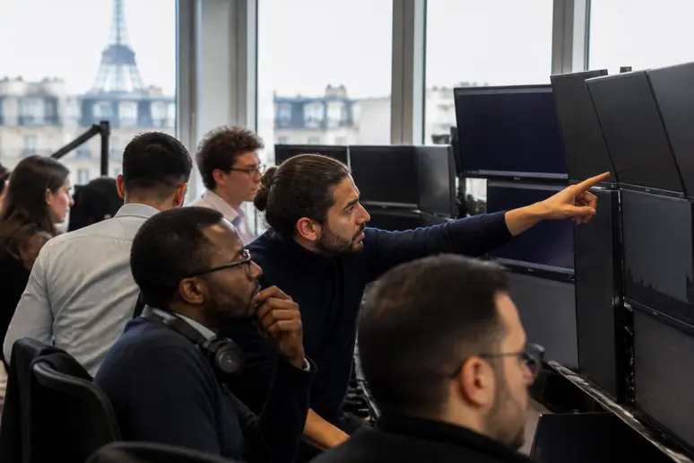 Des traders parisiens analysent des graphiques de cryptomonnaies sur plusieurs écrans, dans une ambiance professionnelle et concentrée.