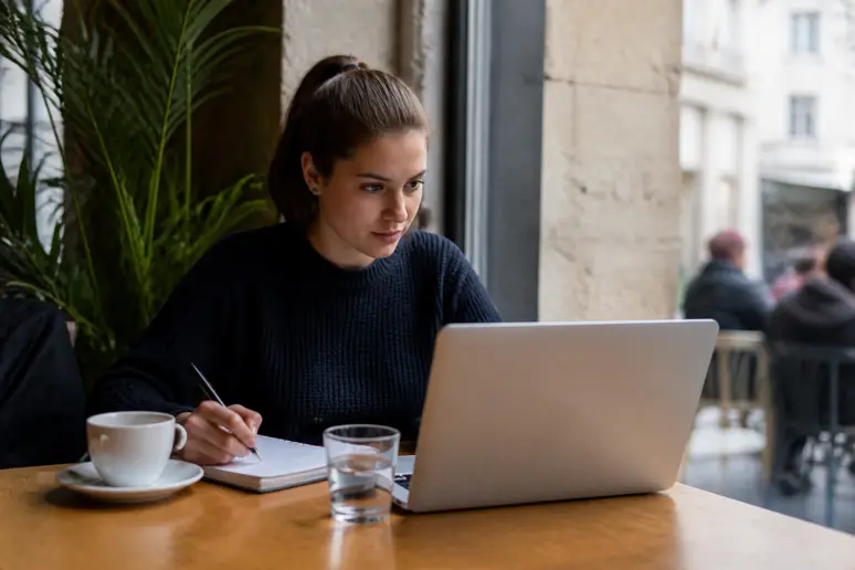 Une jeune Lyonnaise consulte une vidéo éducative sur les cryptomonnaies dans un café, prenant des notes.