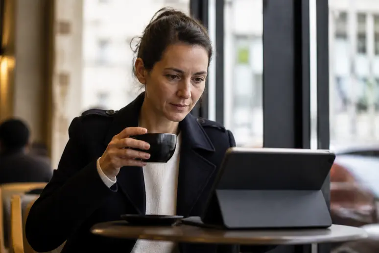 Une femme parisienne analyse des graphiques financiers sur sa tablette dans un café lumineux, illustrant la complexité des investissements.