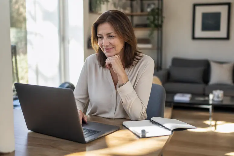 Une femme française consulte des graphiques boursiers sur son ordinateur portable dans son bureau à domicile, ensoleillé et ordonné.