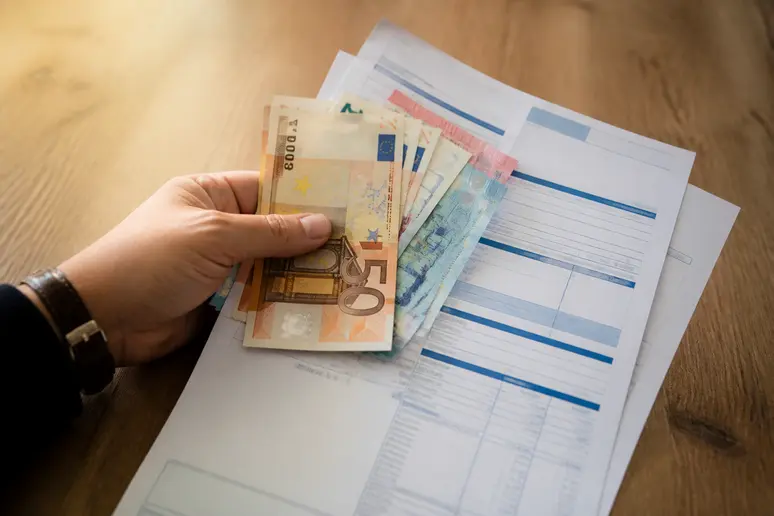 Gros plan sur une main tenant des billets en euros français et un imprimé fiscal, illustrant la fiscalité des investissements.