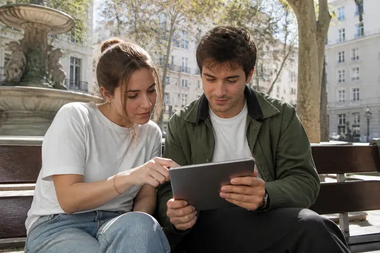 Deux jeunes Français discutent de formation boursière sur une tablette dans un parc à Lyon.