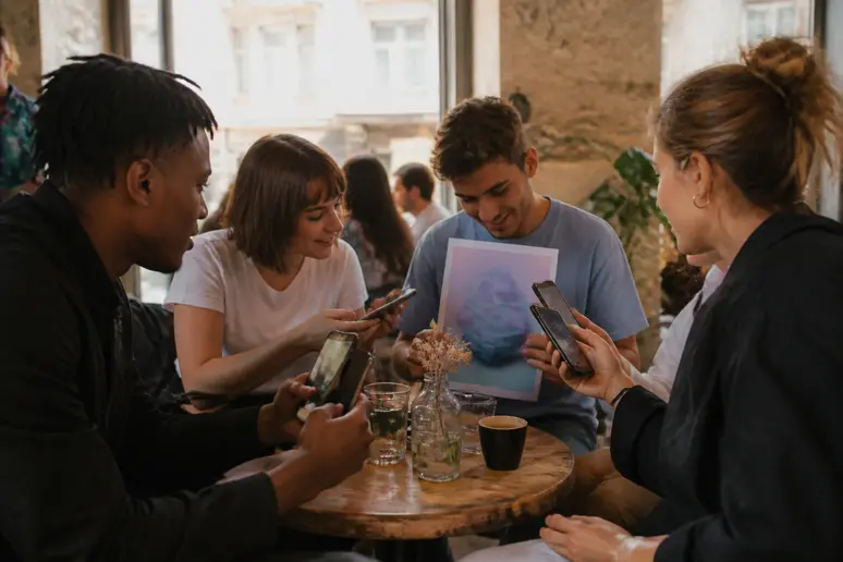 Des jeunes adultes dans un café lyonnais échangent sur leurs smartphones des images d'objets de collection numériques NFT uniques et vérifiables.