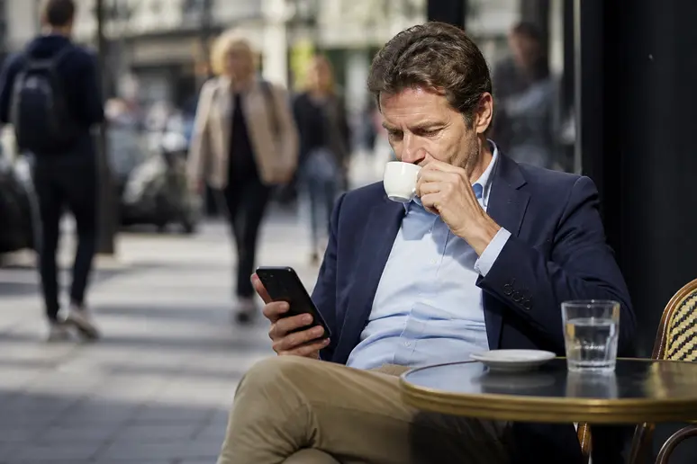 Homme d'affaires parisien examinant des risques liés à la polkadot crypto sur son smartphone, ambiance de café.